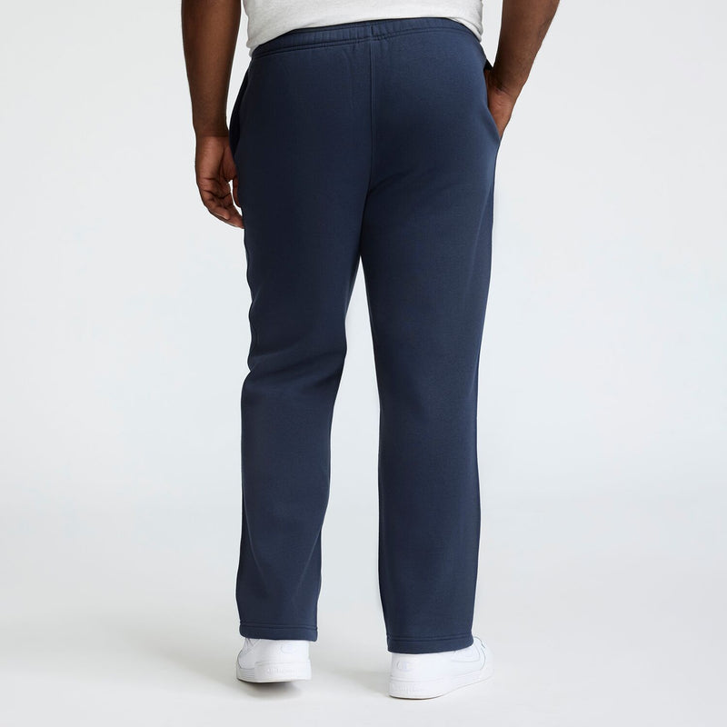 A person is seen from behind in Champion Powerblend Sweatpants, Open Hem, C Logo - Big & Tall, dark blue, paired with white sneakers, standing against a plain light background.