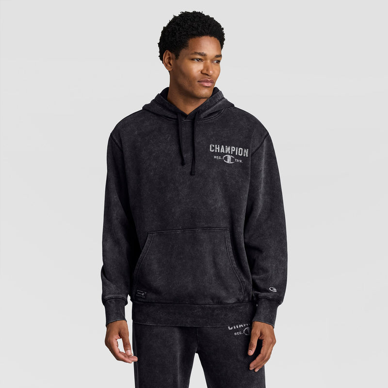 A man wears a black Mineral Wash Pullover Hoodie, C Patch Logo featuring a front kangaroo pocket and a distressed graphic logo on the chest.