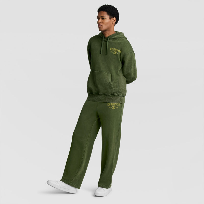 A person wearing an olive green hooded sweatshirt and matching Champion Mineral Wash Open Hem Pant, both featuring gold logo text.