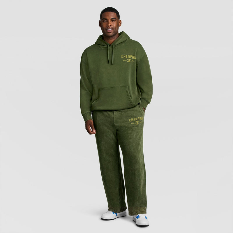 A person wearing a matching olive green hooded sweatshirt and Mineral Wash Open Hem Pant, both featuring gold logo text.