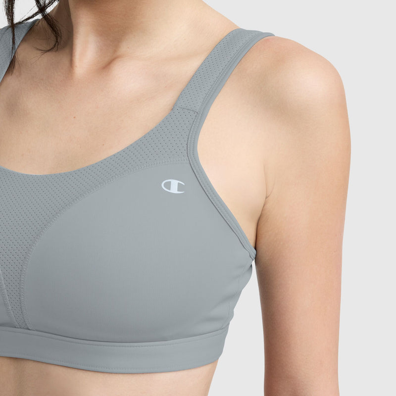 A woman wears the Champion Spot Comfort High-Impact Sports Bra in light gray with a small white C logo on the left, shown from shoulders to just below the bust against a plain light background.