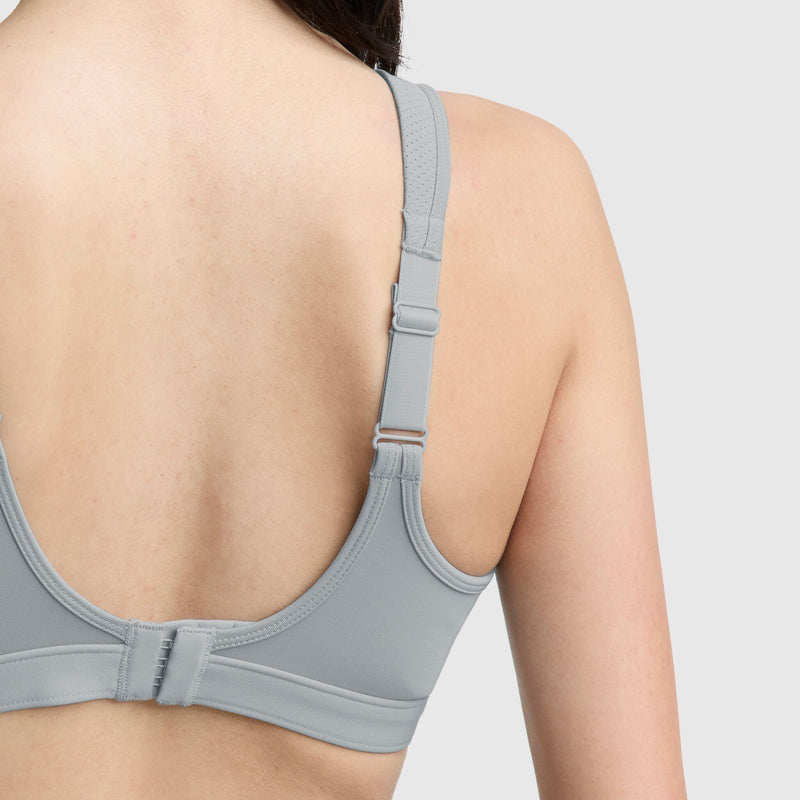 A close-up of a person’s back wearing the Champion Spot Comfort High-Impact Sports Bra, C Logo, in light gray with adjustable straps and hook-and-eye closure, designed for maximum support against a plain background.