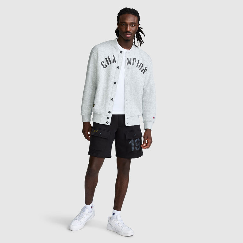 A man wearing a grey vintage Champion Fleece Baseball Jacket over a white t-shirt, black cargo shorts, and white sneakers.