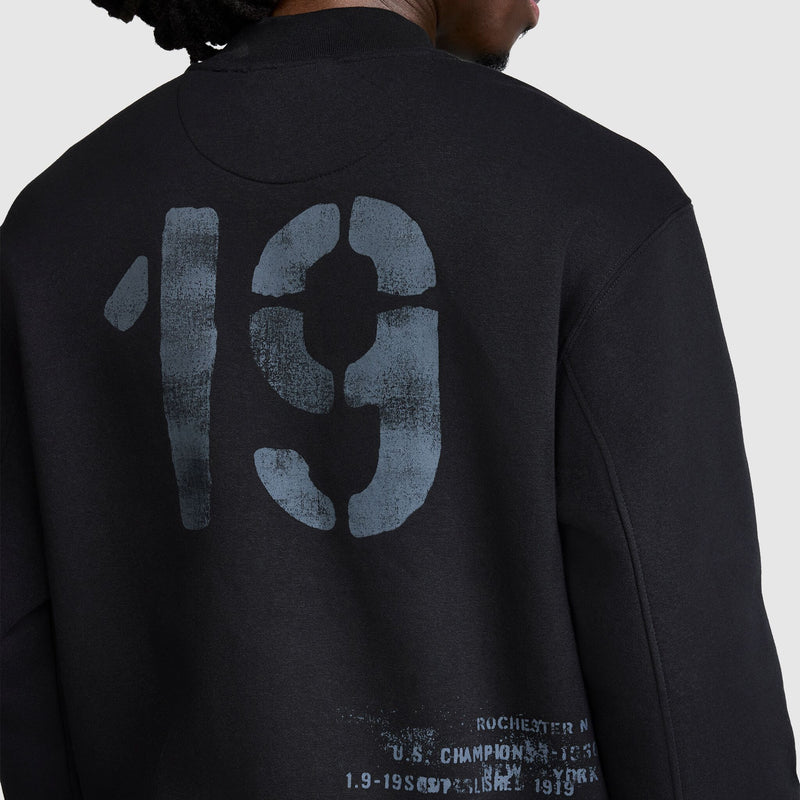 A person is seen from behind wearing the Champion Fleece Baseball Jacket, featuring a large faded number 19 and partially visible white text on the back, channeling a vintage athletic vibe.