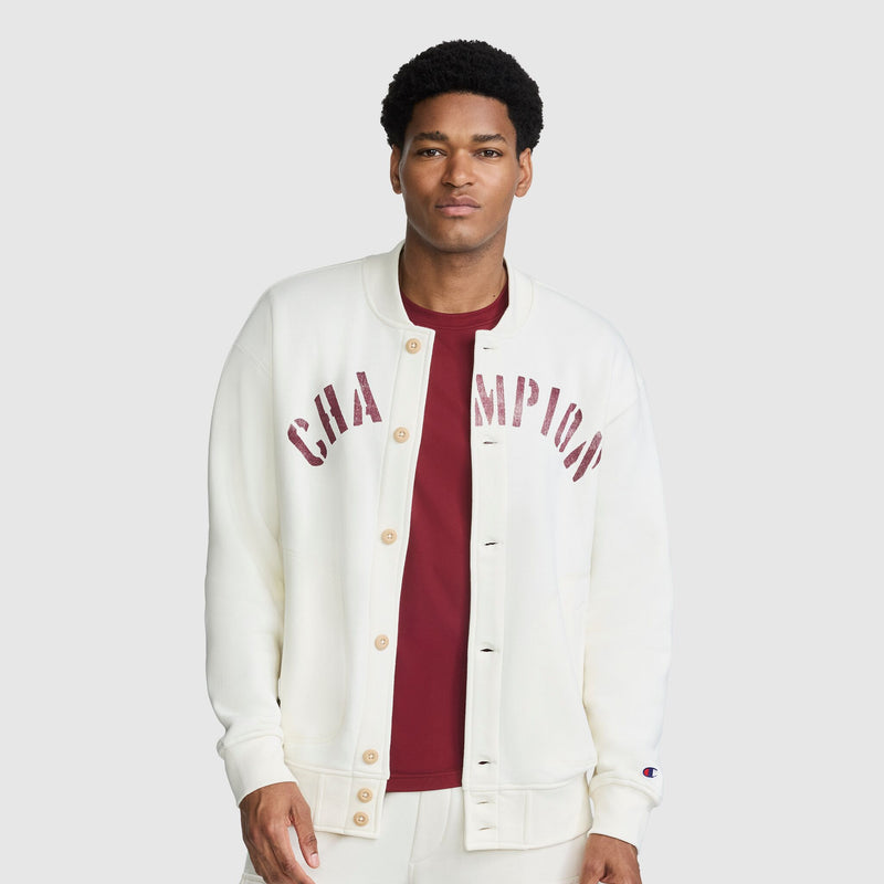 A man wears an off-white Champion Fleece Baseball Jacket with maroon lettering across the chest over a maroon t-shirt.