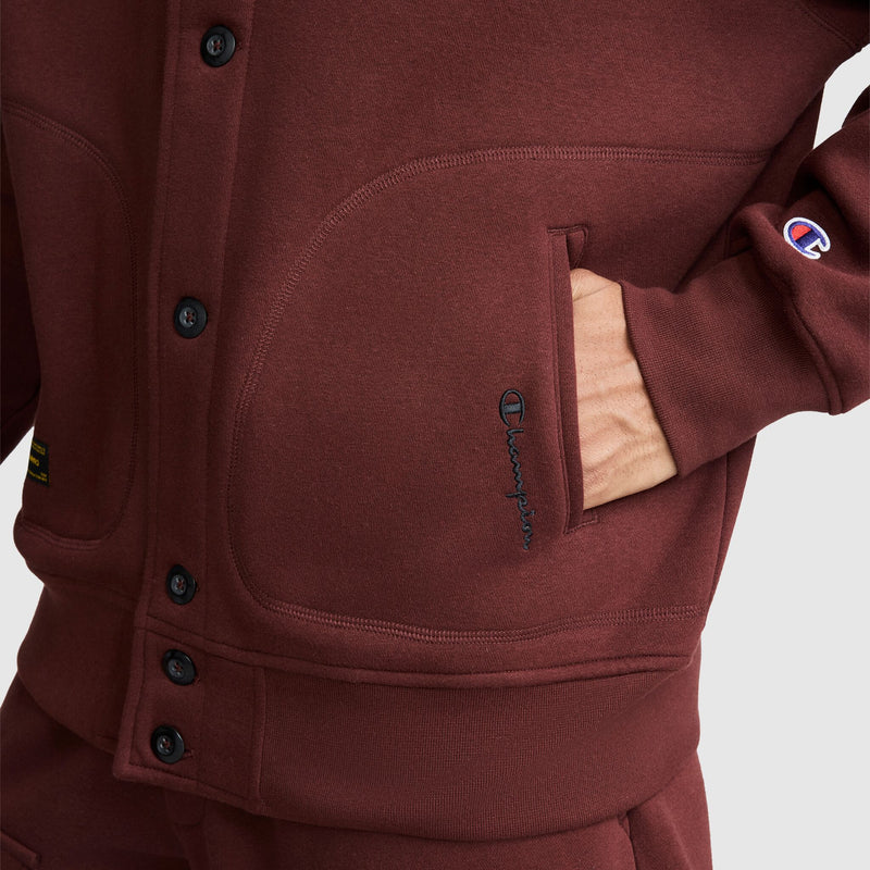 Close-up of a person wearing a maroon Champion Fleece Baseball Jacket with their hand in the side pocket.