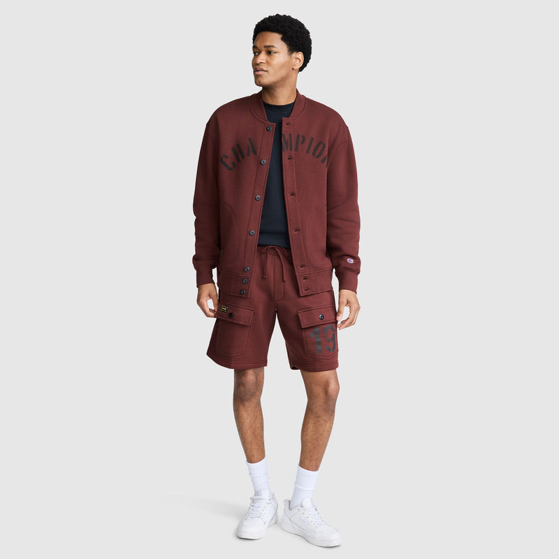 A person wears a maroon Champion Fleece Baseball Jacket with the brand name across the chest and matching cargo shorts with 19 on the leg.