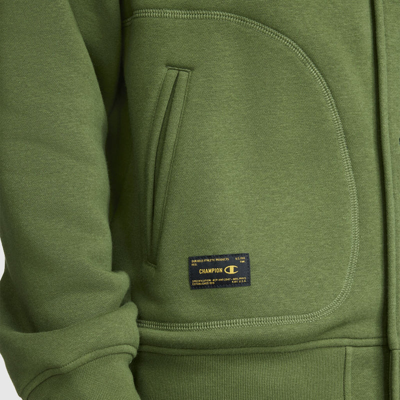 Close-up of a green Champion Fleece Baseball Jacket inspired by vintage athletic style, highlighting a side pocket, ribbed cuff, and a small rectangular Champion brand label near the pocket.