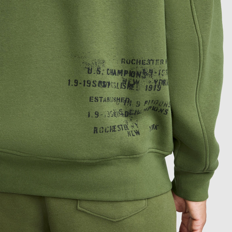 Close-up of a person wearing green Champion Fleece Baseball Jacket featuring faded black text and numbers printed along the side near the waist, channeling a vintage athletic vibe reminiscent of classic varsity jacket styles.