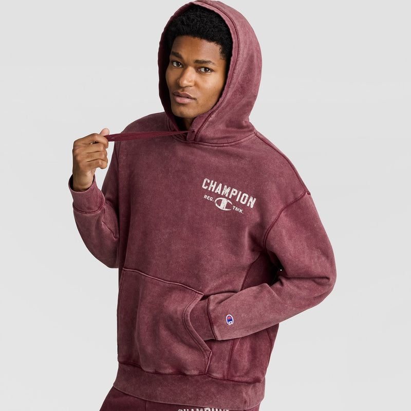 A person wearing a maroon Mineral Wash Pullover Hoodie, C Patch Logo with the hood up and a logo printed on the chest.