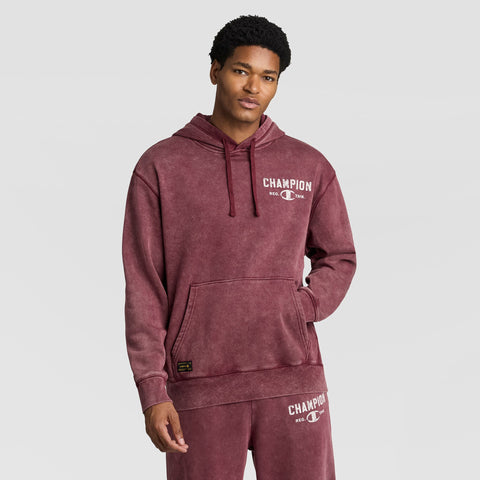 A man wears a burgundy Mineral Wash Pullover Hoodie, C Patch Logo and matching sweatpants, both featuring distressed white logo text on the chest and thigh.