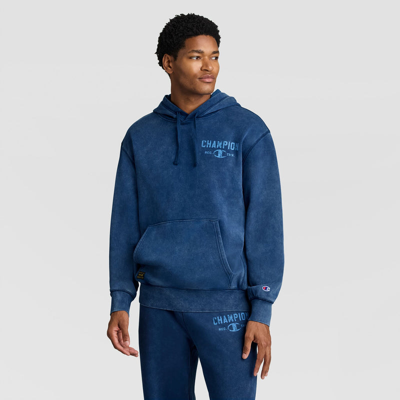 Man wearing a blue Mineral Wash Pullover Hoodie, C Patch Logo and matching sweatpants, both featuring vintage-style logo graphics.