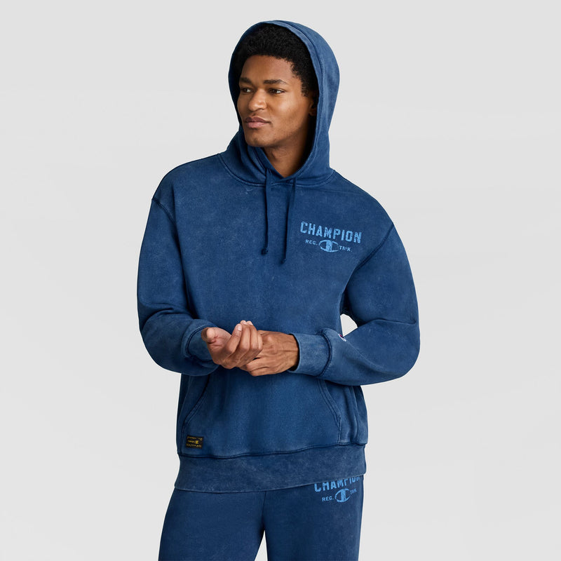 A person wearing a blue Mineral Wash Pullover Hoodie, C Patch Logo with a logo on the chest and a patch on the sleeve.