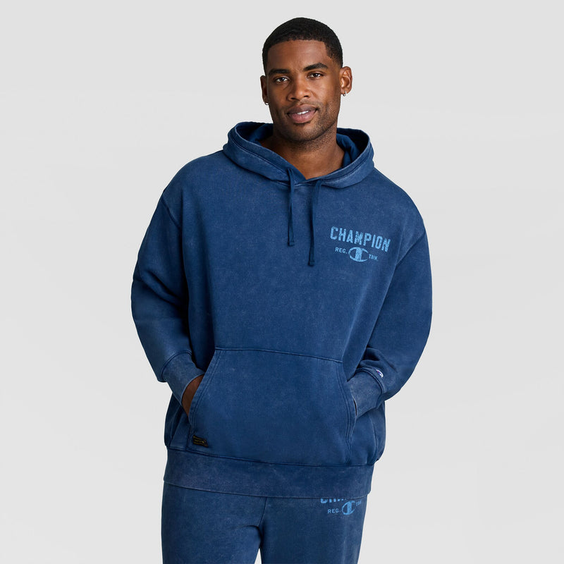 A person wears a blue Mineral Wash Pullover Hoodie, C Patch Logo featuring a chest logo and a kangaroo pocket.