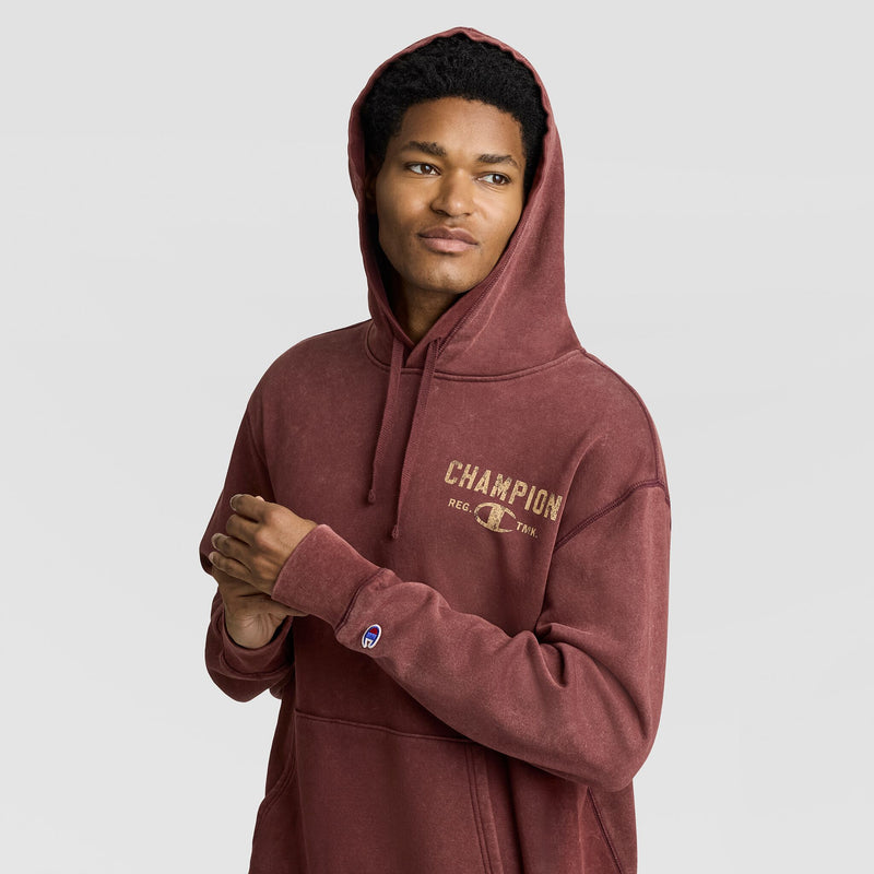 A man wearing a burgundy vintage Mineral Wash Pullover Hoodie, C Patch Logo with a distressed-style logo on the chest and a small patch on the sleeve.