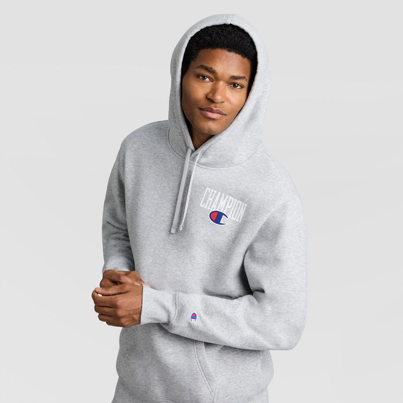 A person wearing a grey Champion Fleece Hoodie, Left Chest Graphic, featuring a logo on the left chest and a small patch on the wrist.