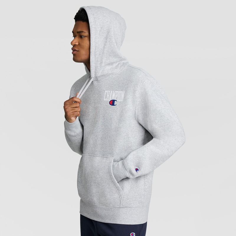A person wearing a grey Champion Fleece Hoodie, Left Chest Graphic, featuring a logo on the left chest and a small patch on the sleeve.