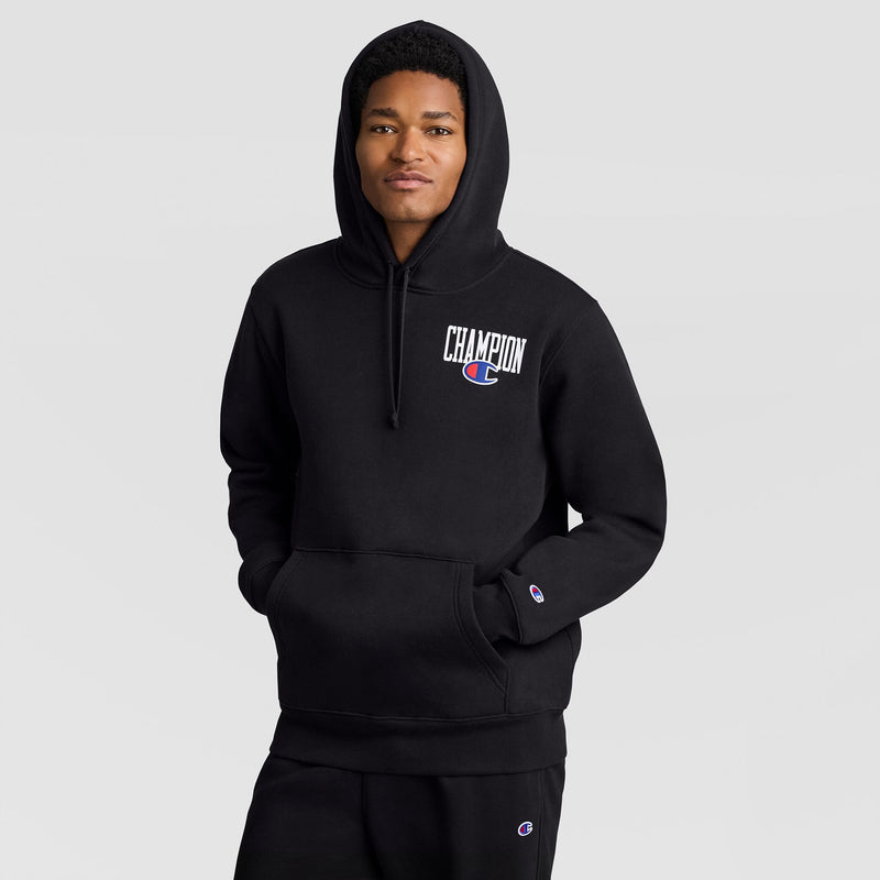 A person wearing a black Champion Fleece Hoodie, Left Chest Graphic with a white and blue logo on the left chest and hands in the front pocket.