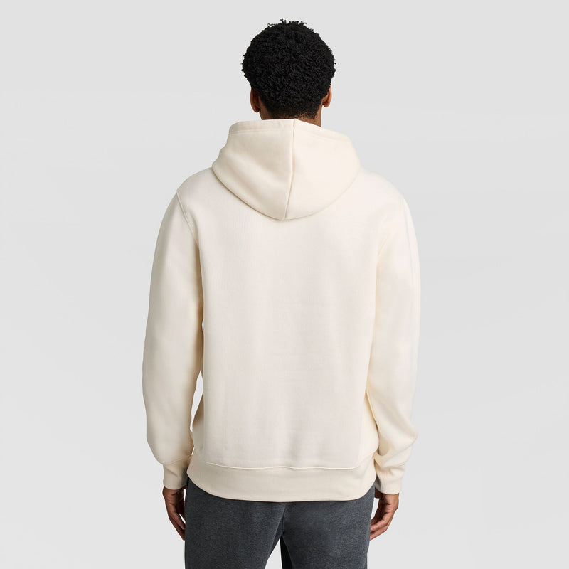 Back view of a person wearing a cream-colored Champion Fleece, Left Chest Graphic hoodie and dark gray pants.
