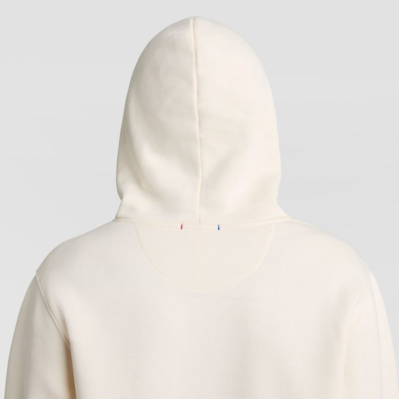 Back view of an off-white Champion Fleece Hoodie, Left Chest Graphic, featuring a small red and blue stitch detail at the base of the hood.