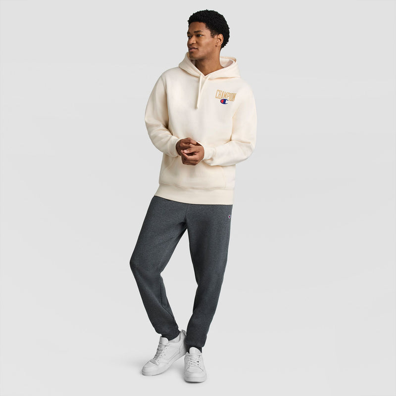 A person wearing an off-white Fleece Hoodie, Left Chest Graphic by Champion and dark gray sweatpants.