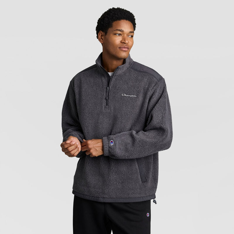 A person wears a charcoal grey Champion Polar Fleece Quarter Zip featuring smooth shoulder panels and a drawstring hem.