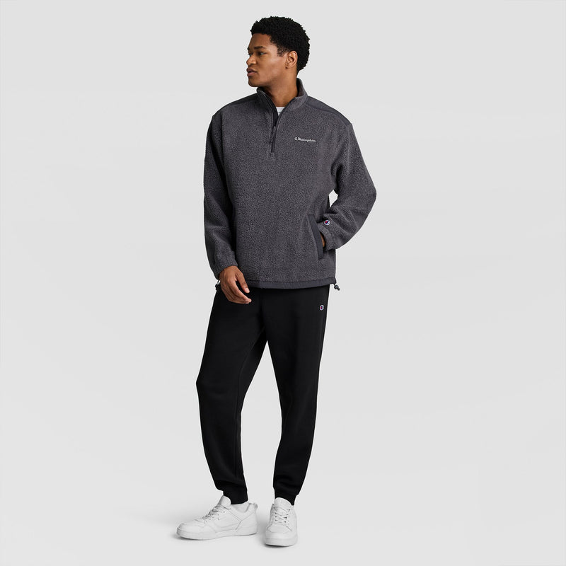 A man wearing a charcoal grey Champion Polar Fleece Quarter Zip, black sweatpants, and white sneakers.