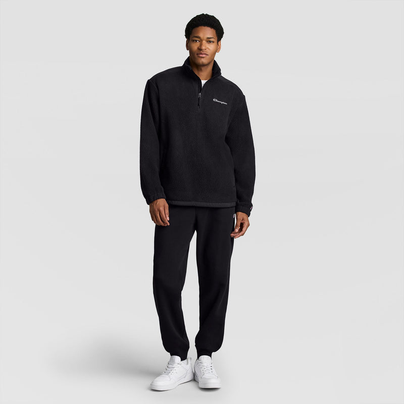 A person wearing a black Champion Polar Fleece Quarter Zip quarter-zip pullover and black sweatpants with white sneakers.