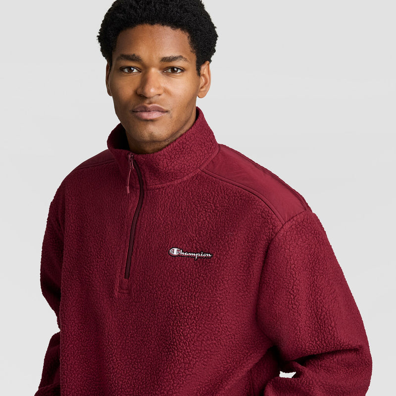A man wearing a burgundy Champion Polar Fleece Quarter Zip pullover with a high collar and a chest logo.