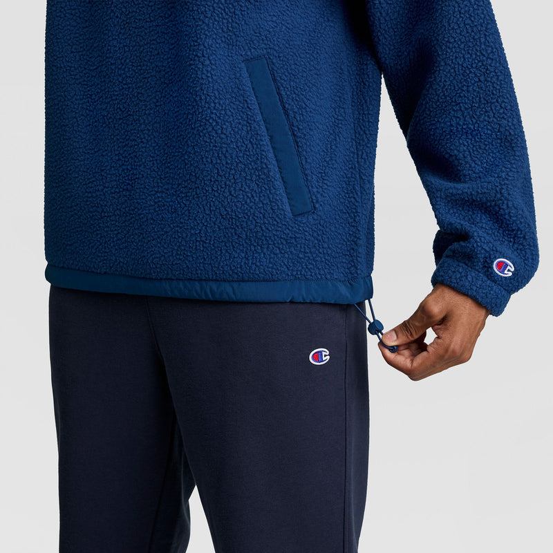 A person wears a blue Champion Polar Fleece Quarter Zip with side pockets and an adjustable drawstring hem, paired with dark blue sweatpants as a cold weather essential.