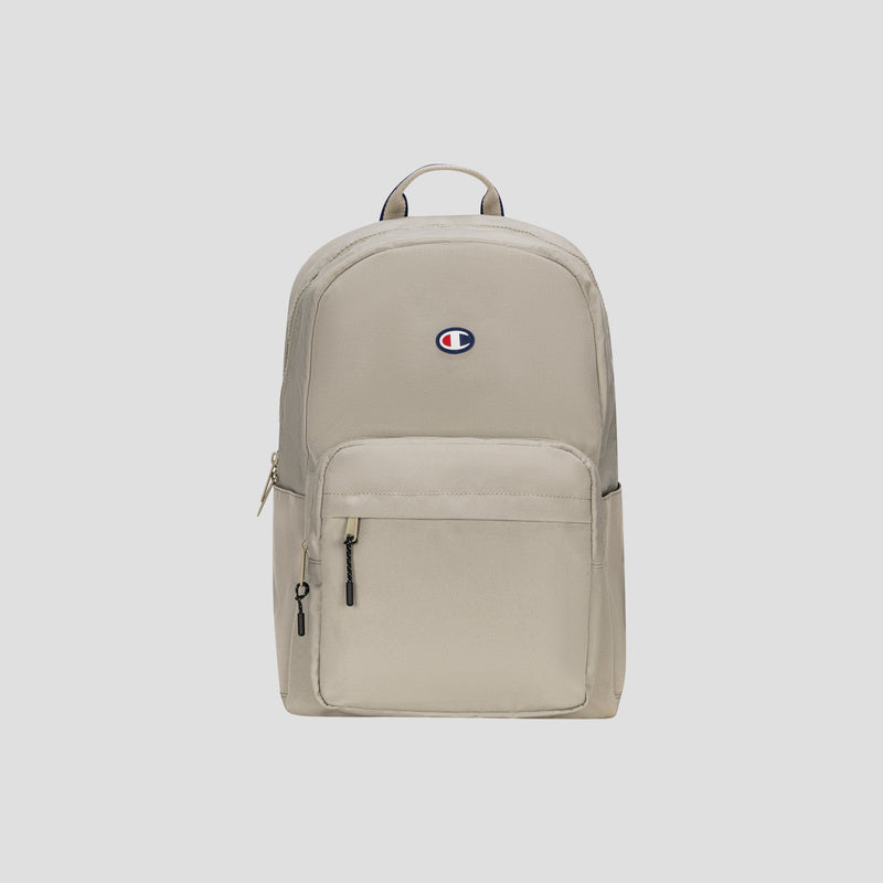 Level Backpack by Champion in beige, featuring a front zipper pocket, small top handle, and the Champion logo in blue, red, and white centered on the upper front. Designed for everyday carry, this backpack includes a padded laptop sleeve for added convenience. Set against a light gray background.