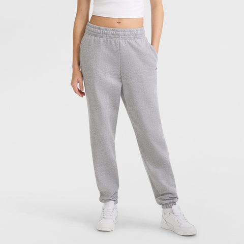 A person stands against a plain white background wearing a white crop top, Champion Powerblend Oversized Sweatpants with C Logo in light gray, and white sneakers. Their head is not visible.