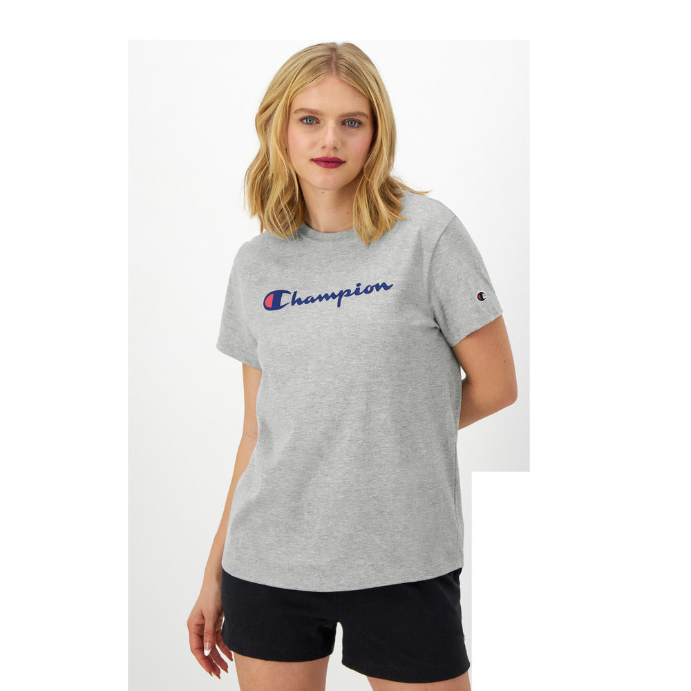 A woman with blonde hair wears the Champion Classic T-Shirt with script logo and black shorts, standing against a white background and looking at the camera with a neutral expression.