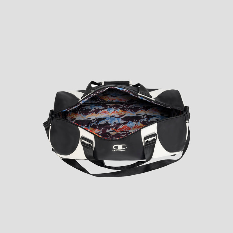 A black and white Oracle Duffel Bag by Champion with the top unzipped, revealing a colorful, abstract-patterned interior lining. This versatile sports bag offers both a shoulder strap and handles, and showcases the iconic Champion logo on the front.
