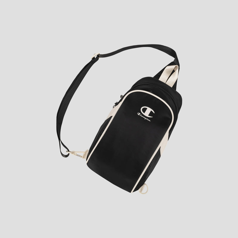 The Oracle Sling Pack by Champion is a black and beige crossbody bag featuring an adjustable strap and a white Champion logo on the front, displayed against a light gray background. Ideal as a gym bag or for everyday use.