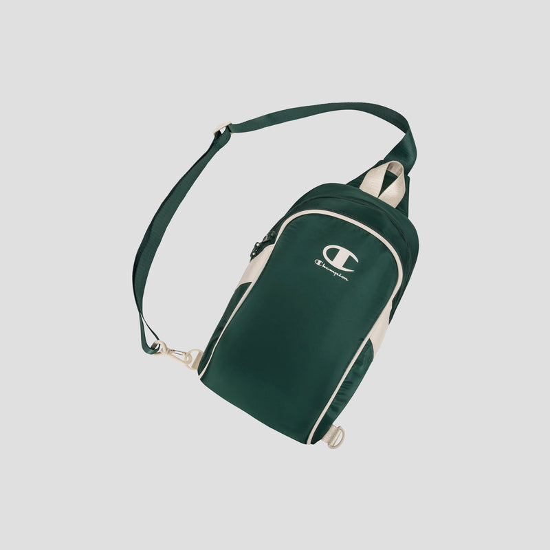 The Champion Oracle Sling Pack in dark green and beige features an adjustable shoulder strap, zippered compartments, and the Champion logo prominently displayed on the front. The bag is shown against a plain white background.