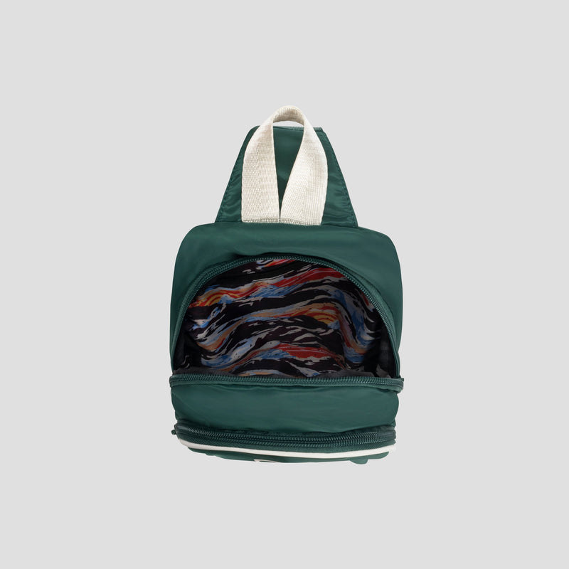 The Champion Oracle Sling Pack in small green is pictured open, displaying its vibrant abstract-patterned lining and cream-colored straps against a light gray background.