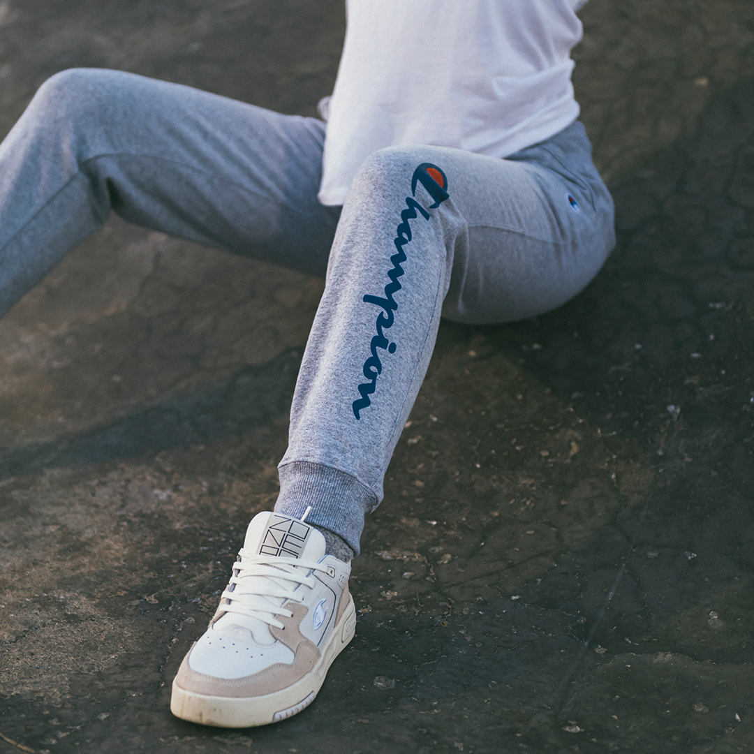 Person wearing gray sweatpants with a logo and white sneakers on a skate park ramp