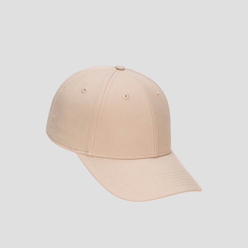 A Champion Ponytail Baseball Cap, made from performance stretch fabric in plain beige, is displayed against a light gray background and angled to the left.