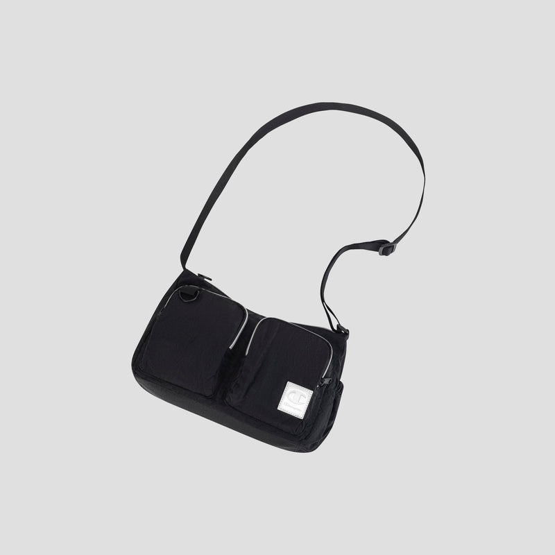 The Champion Quartz Small Messenger Bag is a lightweight nylon crossbody in black, featuring two front zip pockets, an adjustable strap, and a small white rectangular patch on the lower right front, displayed against a plain light gray background.