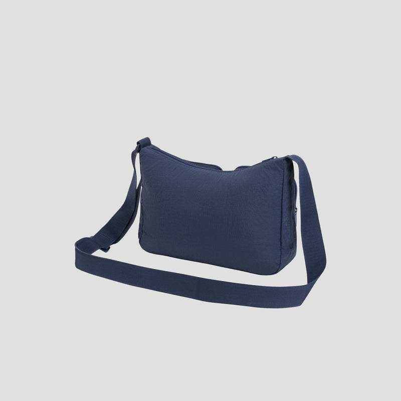 The Champion Quartz Small Messenger Bag, crafted from lightweight navy blue nylon, features a long adjustable strap, zippered top closure, and a simple design. It is displayed against a plain light gray background.
