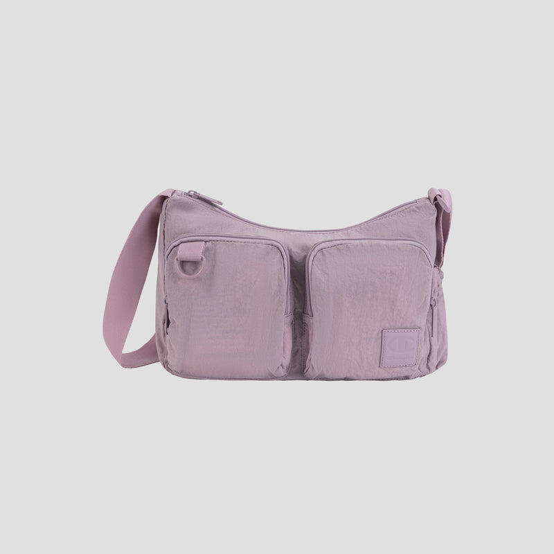 The Champion Quartz Small Messenger Bag, shown here in light purple and crafted from lightweight nylon, features two front zippered pockets, a long adjustable strap, and a small rectangular patch on the lower right side—perfect for carrying daily essentials while traveling, all displayed against a plain white background.