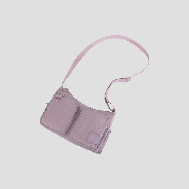 The Champion Quartz Small Messenger Bag is a light purple crossbody featuring two front pockets and an adjustable shoulder strap, shown against a plain white background. Made from lightweight nylon, it’s perfect for travel and everyday use.