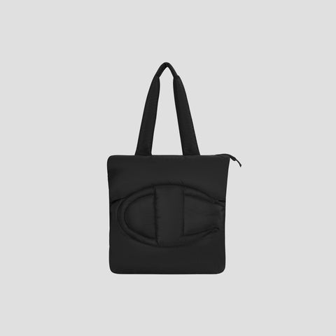 The Champion Quilted Billie Tote features black padded quilting with two handles and a large, rounded stitched design on the front, shown against a plain light gray background—a stylish everyday bag.