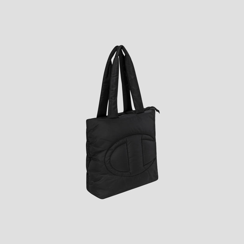 The Champion Quilted Billie Tote features a black quilted design with two long handles and a subtle, large oval pattern stitched on the front, shown against a plain light gray background—perfect for everyday use.