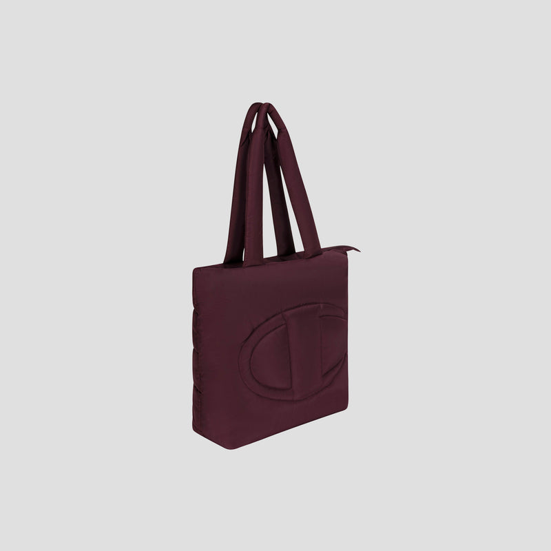 The Champion Quilted Billie Tote is a maroon rectangular bag with double handles and a large embossed oval logo on the front, ideal for everyday use, showcased against a plain light gray background.