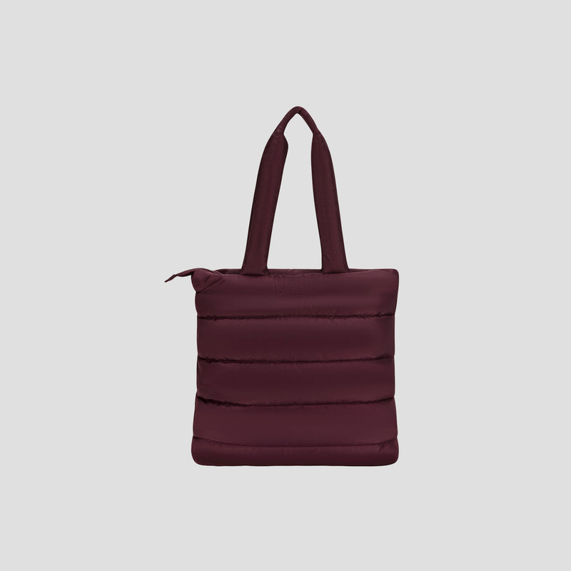 The Champion Quilted Billie Tote is a stylish, dark maroon tote bag featuring padded handles, vertical quilted stitching, and a secure zipper closure—perfect for everyday use. It is displayed against a plain light gray background.
