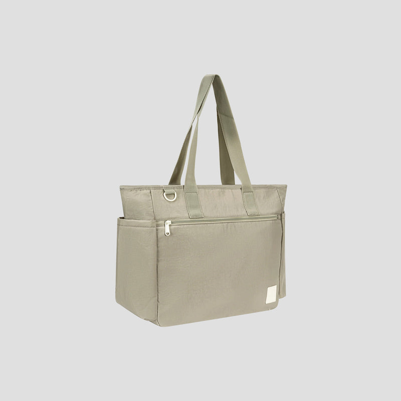 The Champion Quartz East West Tote is a lightweight crinkle nylon bag in light gray, designed with double handles, a zippered front pocket, and handy side pockets. This travel tote stands upright against a plain light gray background and features a padded laptop sleeve to help keep your essentials organized on the go.