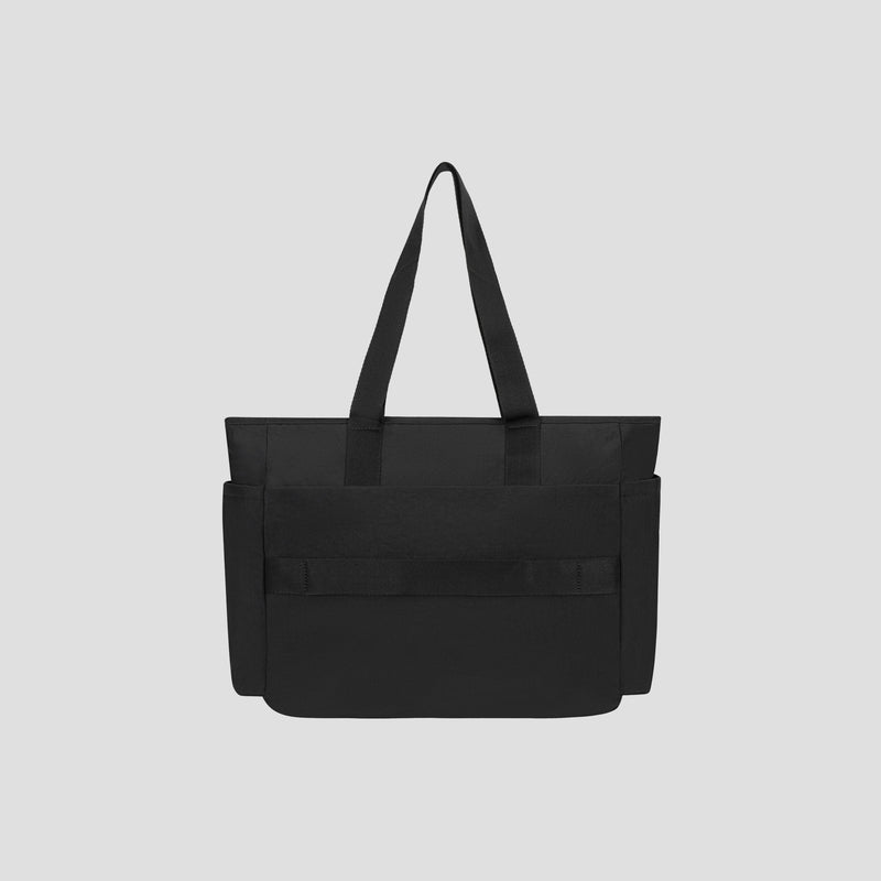 The Champion Quartz East West Tote is a black crinkle nylon bag with two long handles, a front pocket, and side compartments. It features a padded laptop sleeve, making it both stylish and functional for travel. The tote is displayed on a plain light gray background.
