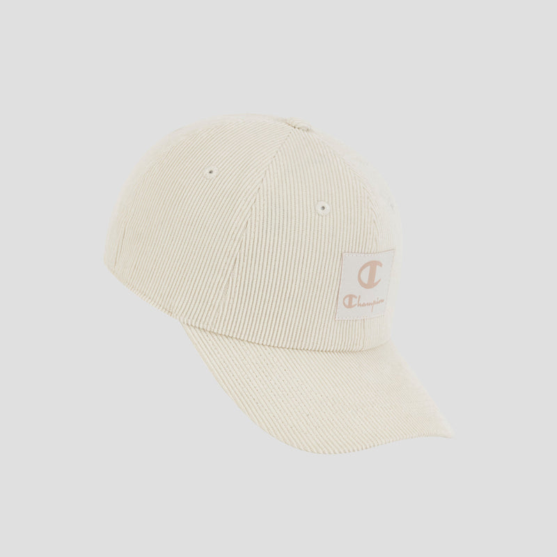 The Ridge Corduroy Adjustable Cap by Champion is a cream-colored, vintage-inspired corduroy hat featuring a curved brim and a Champion logo patch on the front left side, with an adjustable back closure. It is displayed against a plain light gray background.